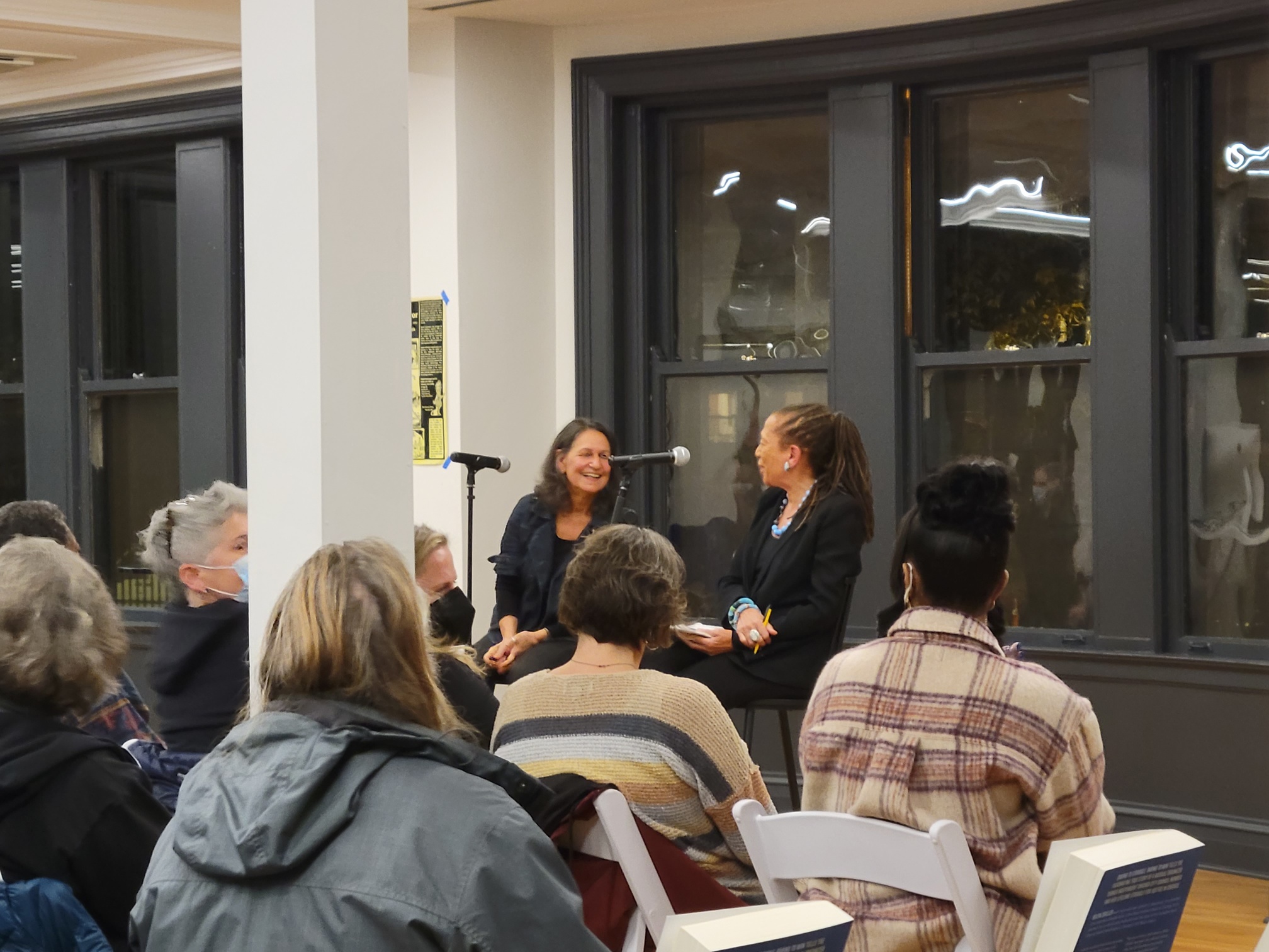 Two panelists talk in front on an audience at Haymarket House.